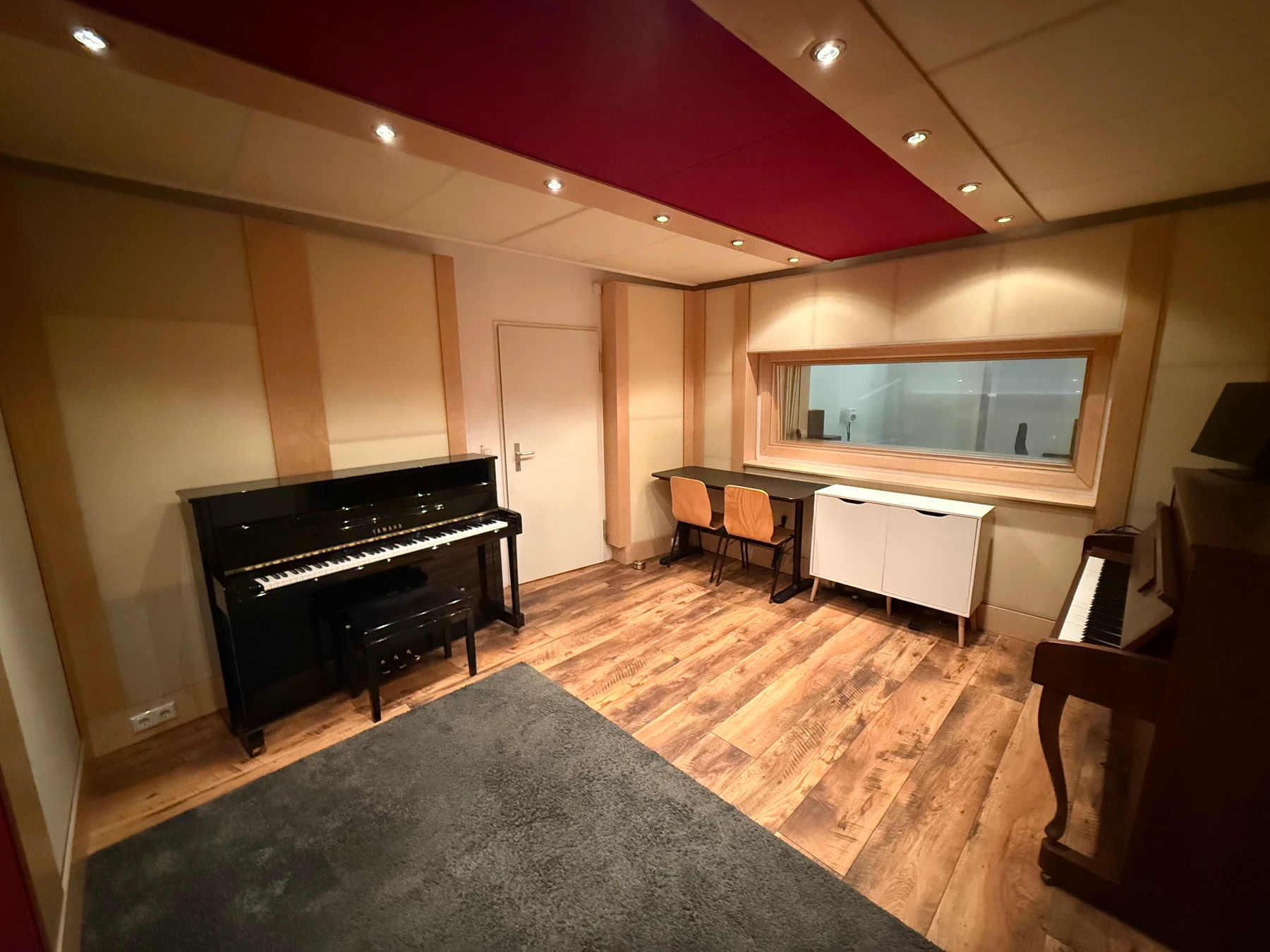Live room overview — upright piano, burgundy carpet, acoustic panels and warm recessed lighting