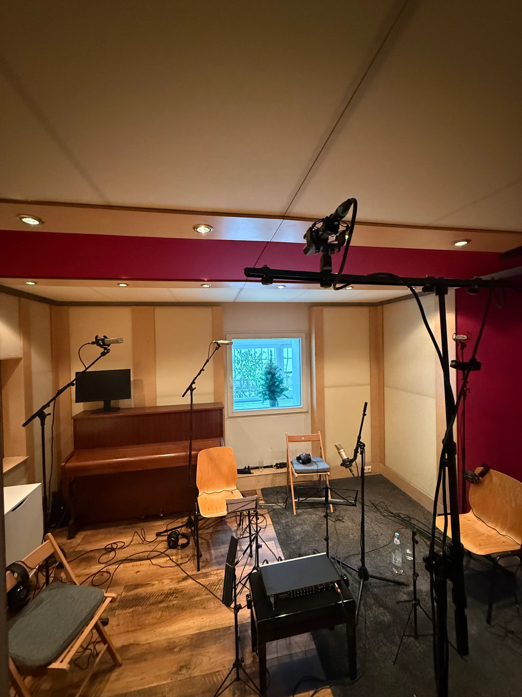 Live room set up for recording — multiple microphone stands, piano, and burgundy accent wall